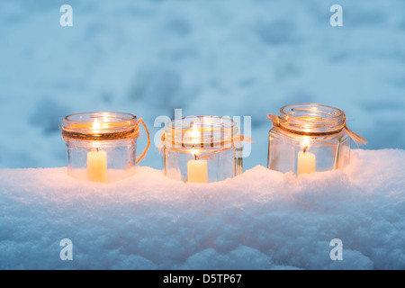 Christmas candles in a glass jars in a snow covered wood Stock Photo