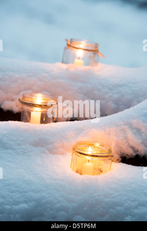 Christmas candles in a glass jars in a snow covered wood Stock Photo