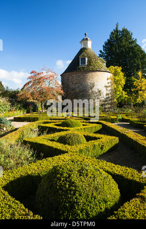 Topiary spheres and box-hedge Parterre with a dogwood tree and 17th-century Dovecote, in early November at Rousham House gardens, Oxfordshire, England Stock Photo