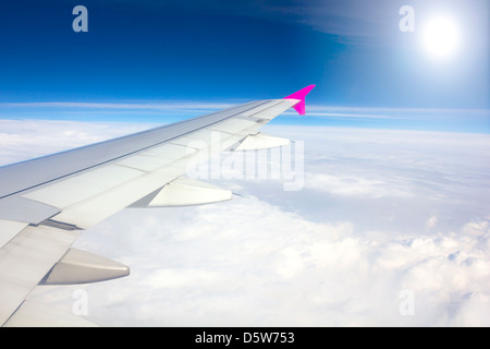 Wing of airplane flying above the clouds with sunlight background Stock Photo