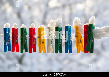 Washing line with a row of colorful pegs covered with snow queued in a row Stock Photo