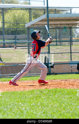 Teen boy baseball player watching ball after his hit. Stock Photo