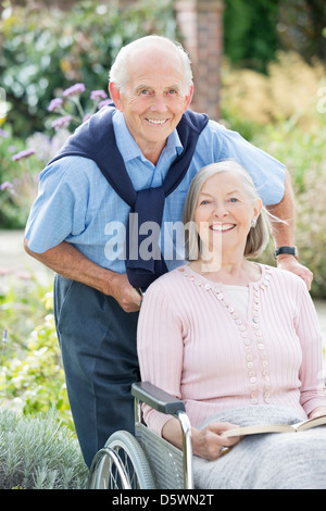 Older man pushing wife in wheelchair outdoors Stock Photo