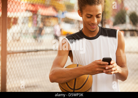 Man using cell phone on basketball court Stock Photo