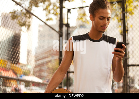 Man using cell phone on basketball court Stock Photo