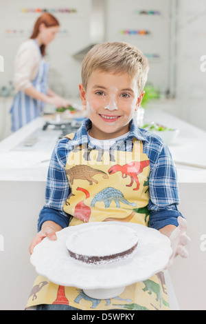 Boy covered in flour holding cake in kitchen Stock Photo