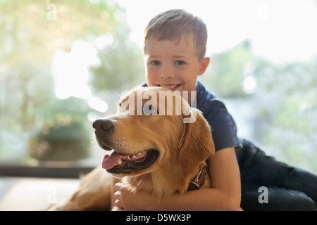 Smiling boy hugging dog indoors Stock Photo