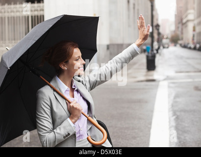 Businesswoman hailing taxi on city street Stock Photo