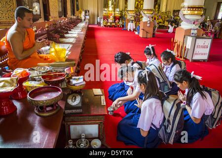 Chiang Mai, Thailand. April 10, 2013. A monk prays with school girls before Songkran at Wat Phra Singh in Chiang Mai. Songkran is celebrated in Thailand as the traditional New Year's Day from 13 to 16 April. Songkran is in the hottest time of the year in Thailand, at the end of the dry season and provides an excuse for people to cool off in friendly water fights that take place throughout the country. The traditional Thai New Year has been a national holiday since 1940, when Thailand moved the first day of the year to January 1. The first day of the holiday period is generally th Stock Photo