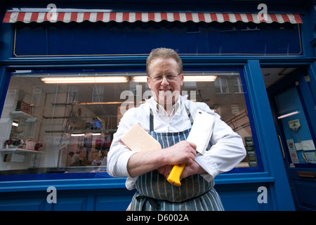 Portrait of  happy senior butcher standing with crossed cleavers in hands outside shop Stock Photo