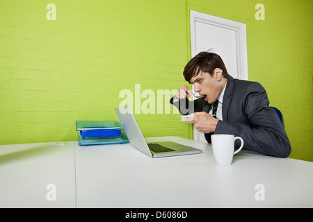 Side view of young businessman eating while using laptop t table Stock Photo
