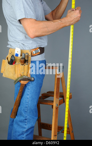Closeup of a contractor standing on a wooden ladder holding a measuring tape. Stock Photo