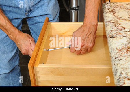 Closeup of a cabinet installer installing drawer hardware on new kitchen cabinets. Horizontal format, man is unrecognizable. Stock Photo