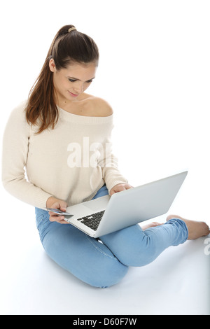 Young Woman, Sitting On The Floor Alone, Working Remote From Her Office Using Laptop Computer Isolated Against A White Background With A Clipping Path Stock Photo