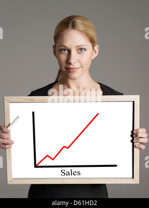 Portrait of young businesswoman showing sales graph gainst gray background Stock Photo