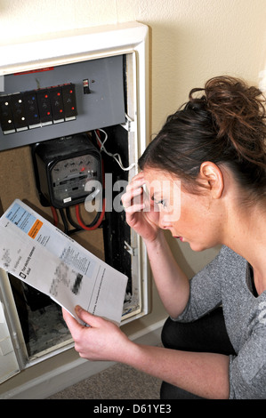 Young woman 20s attempting to read and understand her electricity meter reading and energy bill Stock Photo