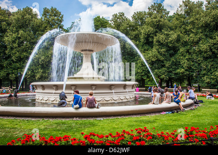People cooling off round the fountain in Ogród Saski, Saxon Garden, the oldest public park in Warsaw, Poland. Stock Photo