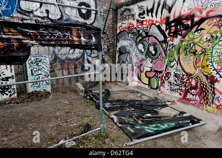 Where young Germans once risked their lives, graffiti and tags now adorn the concrete surfaces of original sections of the Berlin wall at the East Side Gallery on Muhlenstrasse, Berlin. The site is the former border between Communist East and West Berlin during the Cold War. The Berlin Wall was a barrier constructed by the German Democratic Republic (GDR, East Germany) starting on 13 August 1961, that completely cut off (by land) West Berlin from surrounding East Germany and from East Berlin .. (More in Description). Stock Photo