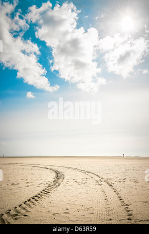 Tire tracks in the sand on the beach of St. Peter-Ording on a sunny day with blue sky and clouds Stock Photo