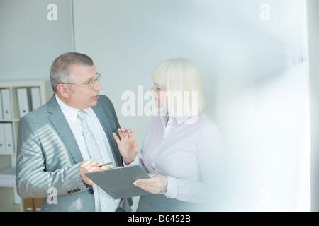 Confident mature businessman and his colleague looking at one another while discussing document at meeting Stock Photo