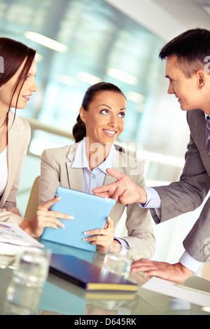 Portrait of three confident employees discussing something in touchpad Stock Photo