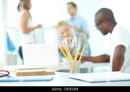 Close-up of several pencils in plastic glass on background of group of students working Stock Photo