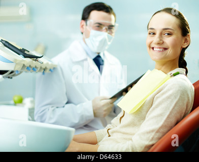 Smiling woman sitting in dentist’s chair with doctor on background Stock Photo