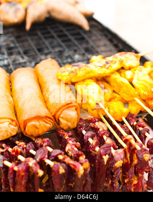 Traditional Thai food at market. Dry beef meat, spring rolls and curry chicken on grill Stock Photo