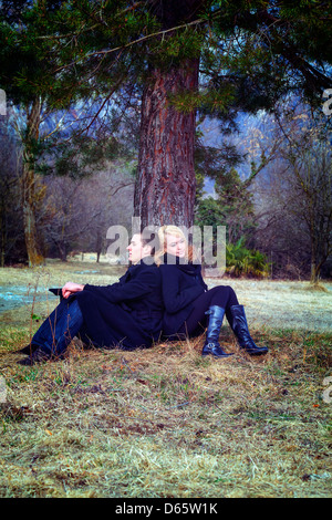 a couple is sitting under a tree Stock Photo