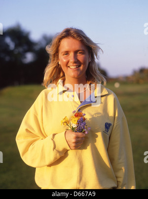 Young woman (20's) holding wild flowers whilst walking, North Devon, England, United Kingdom Stock Photo