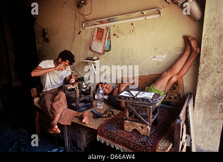 A man is working in a buddhist ritual objects workshop while another craftsman is sleeping in the workplace ( Nepal) Stock Photo