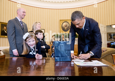 US President Barack Obama signs memorabilia for March of Dimes 2013 National Ambassador Nina Centofanti, 8, at the Resolute Desk during her visit to the Oval Office of the White House March 26, 2013 in Washington, DC. Centofanti's parents Vince and Christine stand behind her. Stock Photo