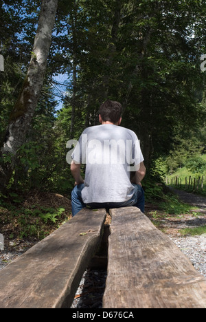 rear view of a young man sitting on wooden bench in the forest Stock Photo