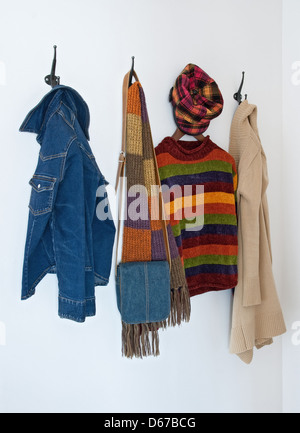 Colorful clothing and bag on metal coat hooks, on a white wall. Stock Photo