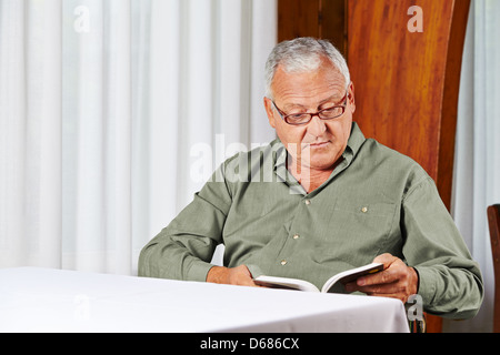 Senior man in rest home reading a book with reading glasses Stock Photo