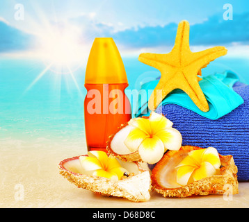 Beach items on sandy coast over blue sea background, sunscreen, yellow starfish, seashell, frangipani flowers Stock Photo