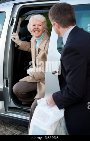 Elderly woman getting out of a taxi with the assistance of a chauffeur. Stock Photo