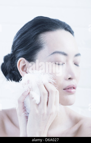 Woman wiping feather on cheek Stock Photo
