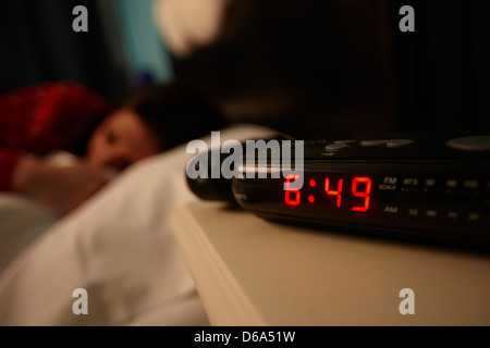 alarm clock early morning with early twenties woman lying in bed in a bedroom Stock Photo