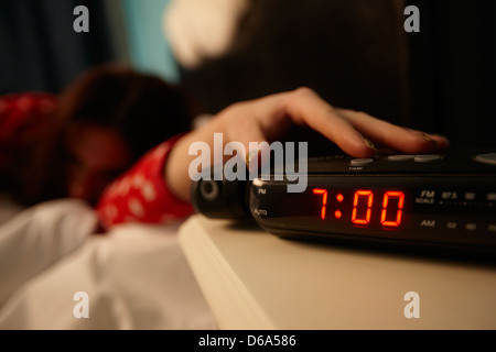 alarm clock early morning with early twenties woman turning off alarm lying in bed in a bedroom Stock Photo
