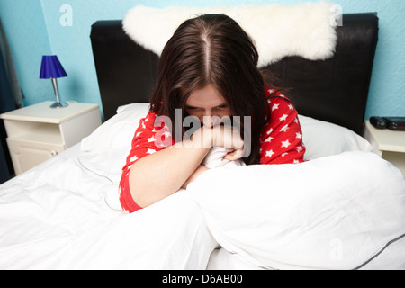 early twenties woman holding duvet tightly in bed in a bedroom Stock Photo