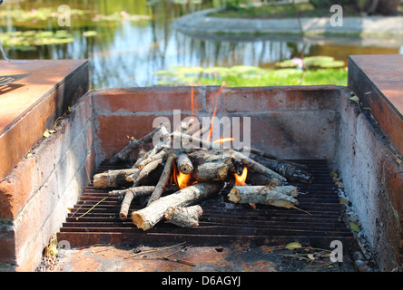 Starting a wood fired oven on a camping trip. Waterpond and nature in the background Stock Photo