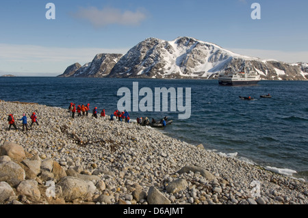 Norway, Svalbard Archipelago, Spitsbergen, St. Johnsfjorden. Cruise ship tourists disembark from a zodiac onto a beach and hike Stock Photo