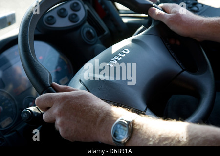 Interior cab view showing hands holding steering wheel of Iveco lorry with part of dashboard visible Stock Photo