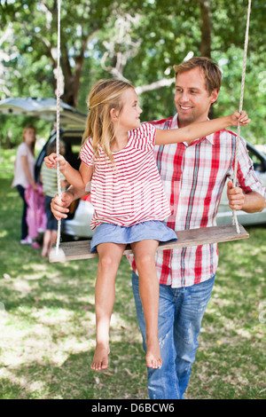 Father pushing daughter on swing Stock Photo
