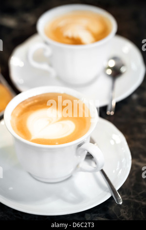 Two white cups of Cappuccino with heart shaped milk foam. Selective focus Stock Photo