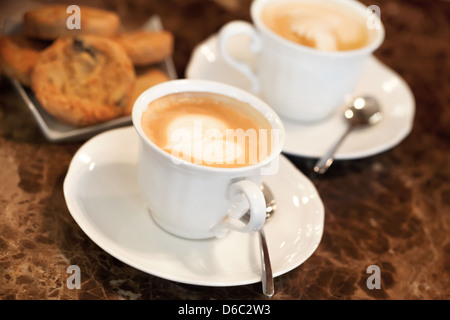 Two white cups of Cappuccino coffee with heart shaped milk foam. Selective focus Stock Photo