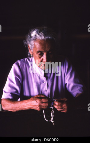 Catholicism in Brazil. Elderly woman prays in church holding a chaplet. Stock Photo