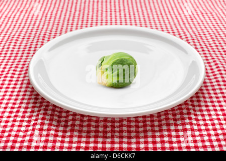 Raw brussels sprouts on white plate on kitchen table, red and white checkered tablecloth in background. Stock Photo