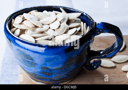 Pumpkin seeds in cup on wooden board Stock Photo